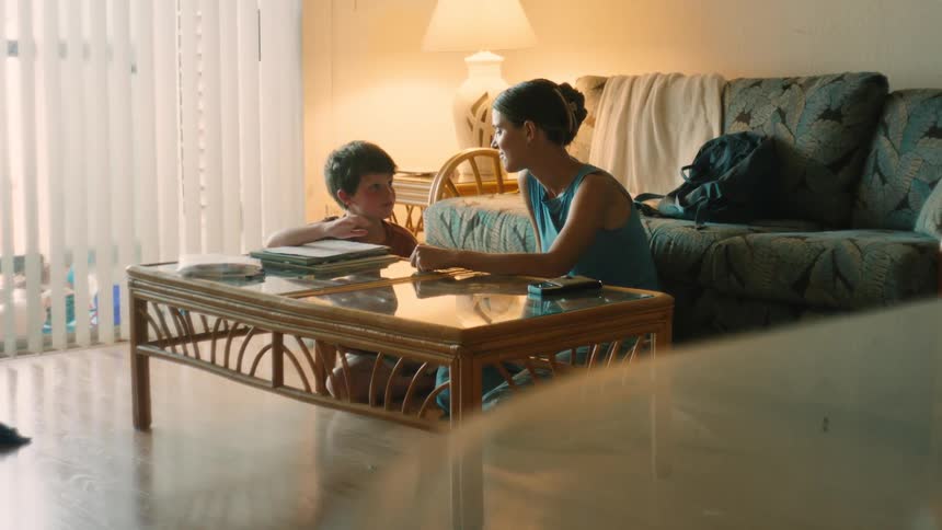 A loving mother helps her young son with his homework in their cozy living room, ending with a celebratory high-five