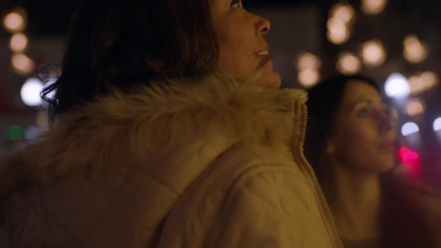 Women standing on a city sidewalk look up at the lights