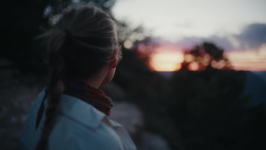 A woman with braided hair contemplates the majestic sunset over a vast and beautiful canyon