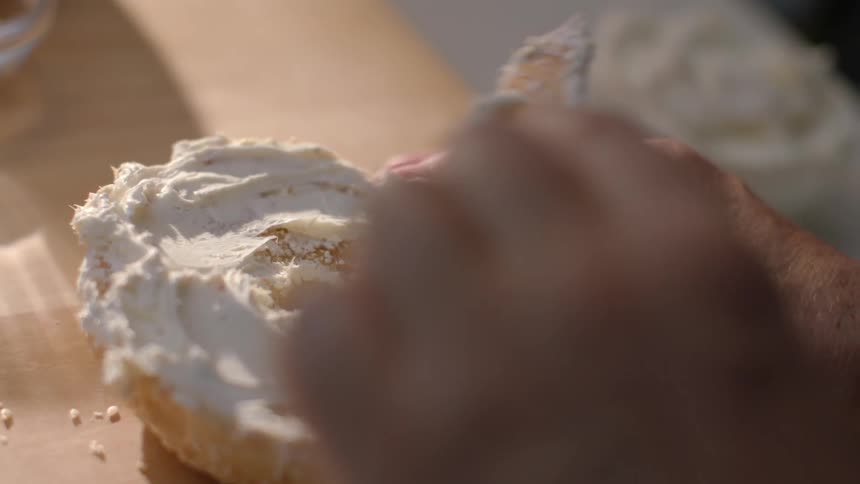 A person puts cream cheese on a bagel