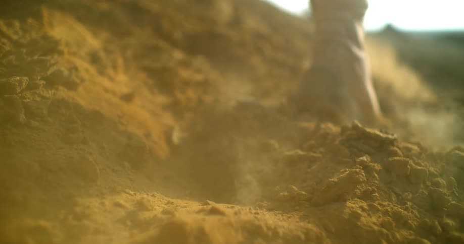 A man kicks up dirt and dust as he walks outside in boots