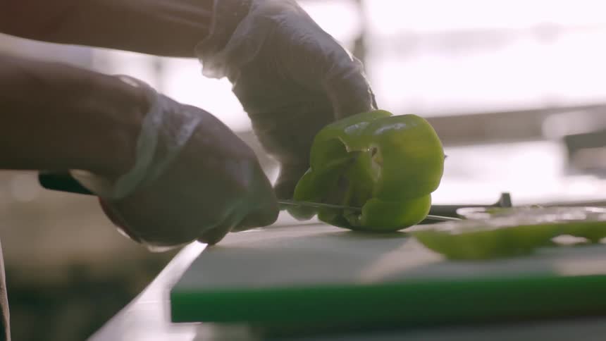Person slicing green pepper on cutting board in kitchen