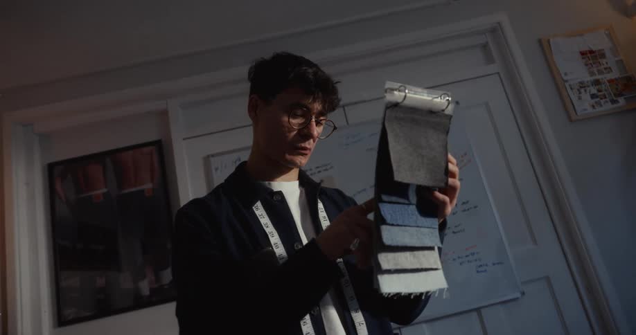 A focused young fashion designer carefully examines a book of denim fabric swatches in his creative studio