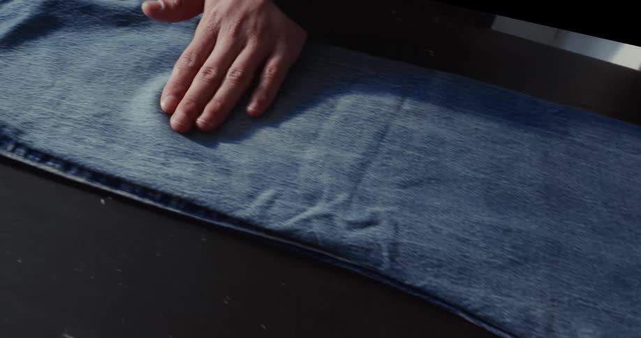A close-up shot of a hand gently feeling the fabric of a pair of blue denim jeans on a dark surface