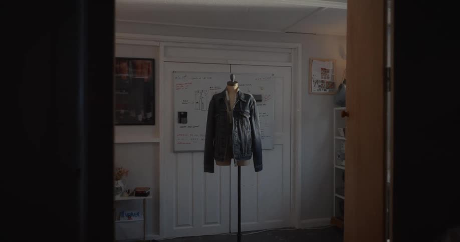 Slow dolly shot reveals a denim jacket on a mannequin in a sunlit fashion designer's studio workshop