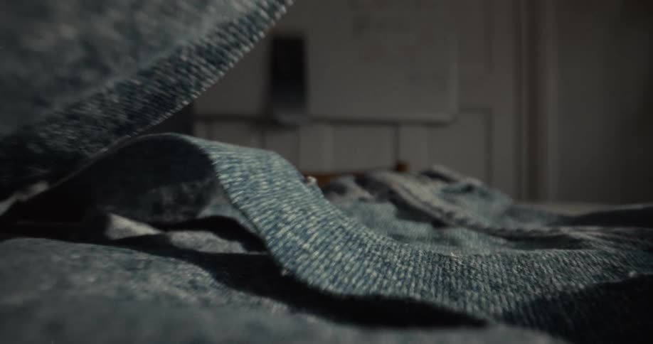 Dramatic macro shot reveals a hand smoothing out a pair of blue denim jeans on a table