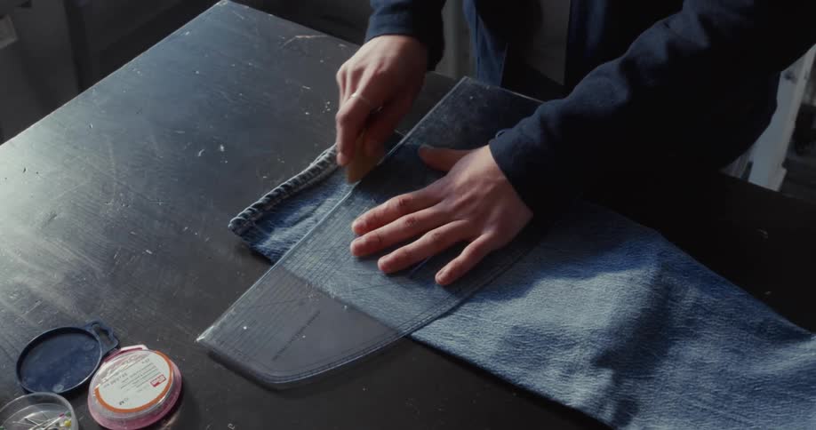 A tailor marks a pair of denim jeans with a pattern and chalk in a workshop