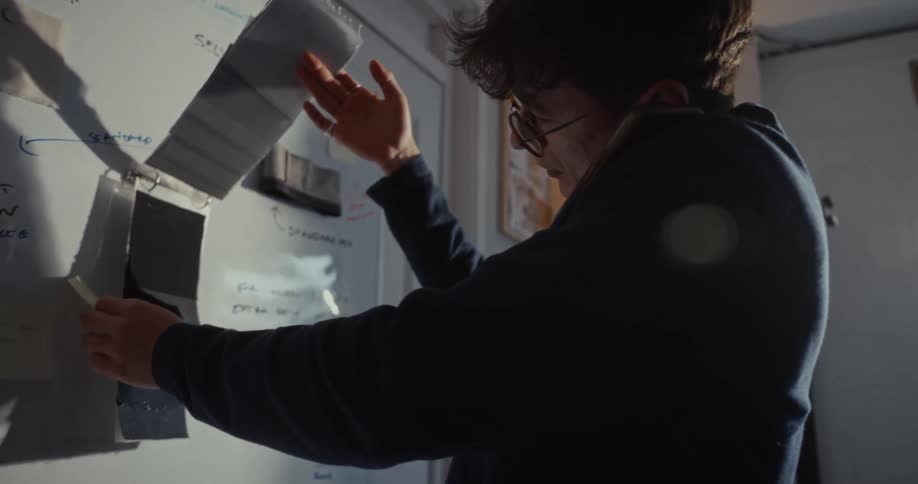 A focused fashion designer on the phone consults his design board, examining fabric swatches and sketches in his studio