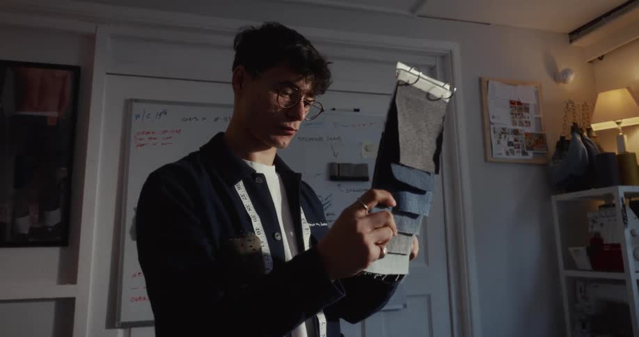 A young fashion designer carefully examines fabric swatches in his creative studio