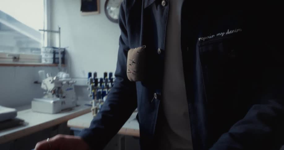 A skilled tailor carefully measures and marks a pair of denim jeans with chalk and a ruler in a slow-motion close-up
