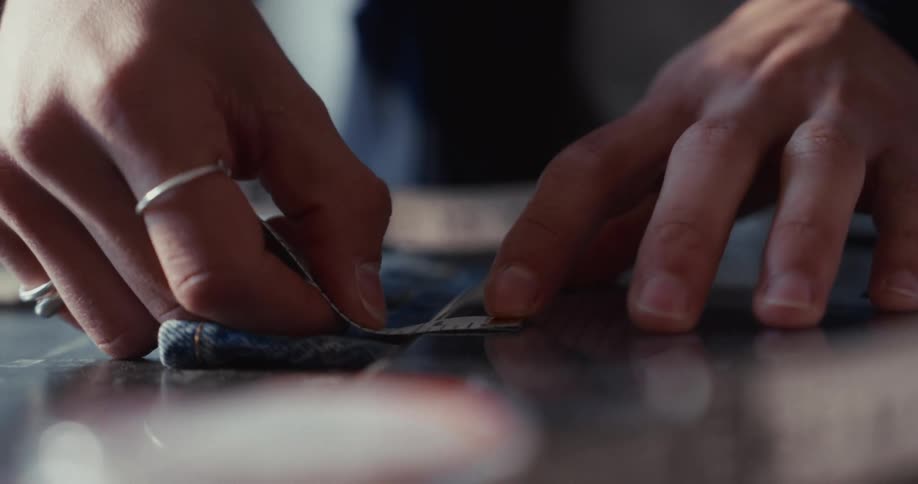 A fashion designer carefully measures a piece of denim fabric with a measuring tape in a workshop