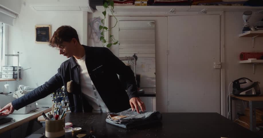 Young male fashion designer meticulously folds a pair of blue jeans for packaging in his workshop