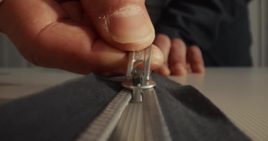 An extreme close-up shot of a hand unzipping the silver zipper on a piece of gray clothing