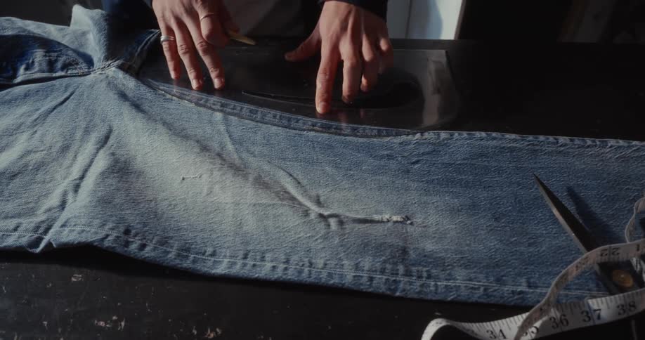 Close up of a fashion designer's hands marking a pattern on blue jeans with chalk and a ruler in a workshop