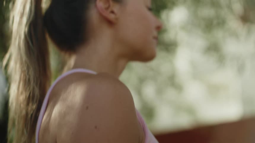 In a slow-motion tilt-up shot, a beautiful woman in athletic clothes stands peacefully in a sunny backyard
