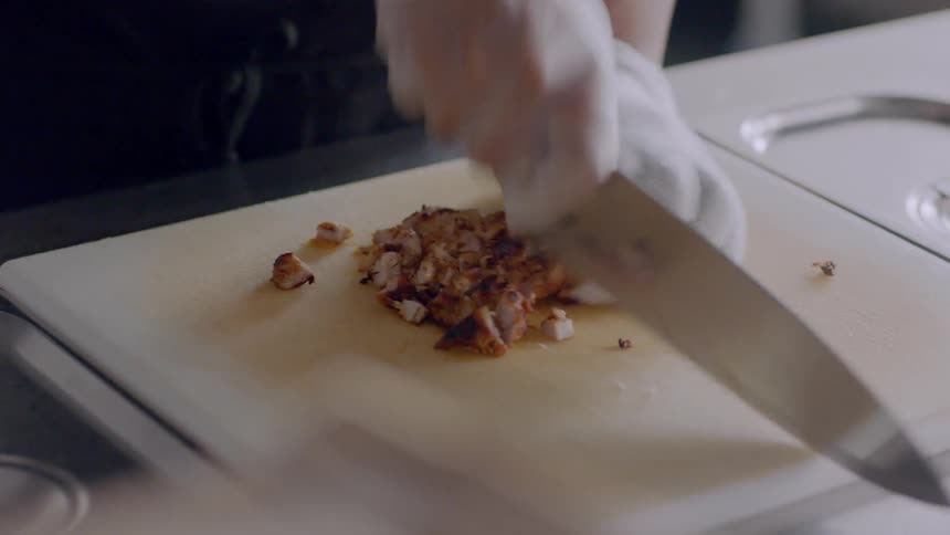 A restaurant worker dices chicken on a cutting board