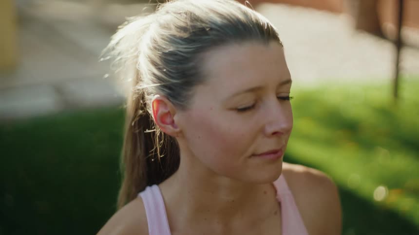 Slow motion close-up of a woman peacefully meditating on a yoga mat in a sunlit backyard