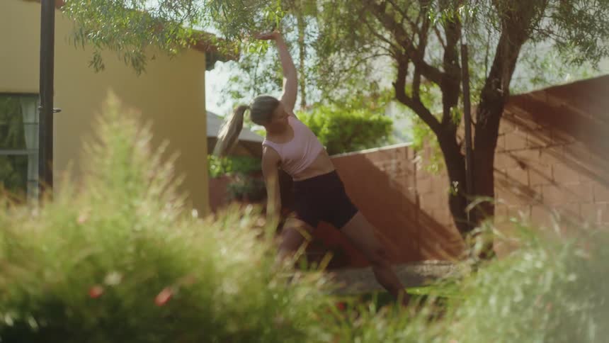 A woman transitions through a series of yoga poses in a lush, sunny backyard, filmed in slow motion
