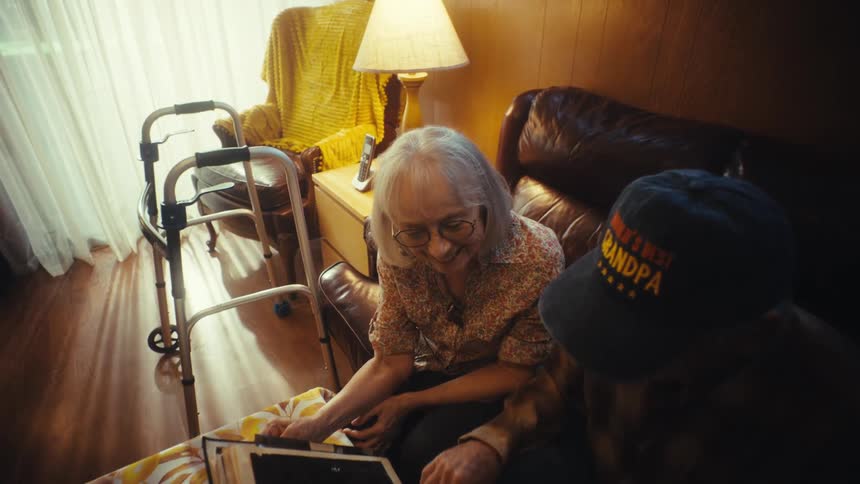An elderly couple smiles and reminisces while looking through a photo album together in their cozy living room