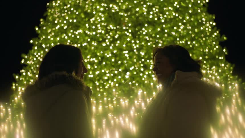 Two women talk in front of a glowing christmas tree