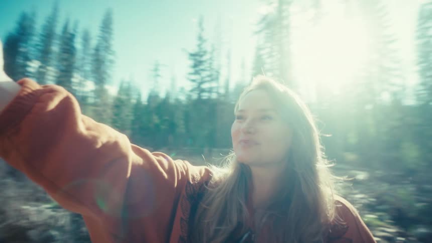 A happy young woman captures a selfie on her smartphone, smiling as she sits in a beautiful sun-drenched forest
