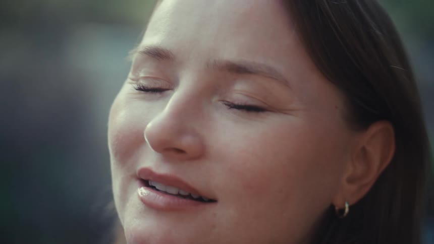 A serene woman with a peaceful smile on her face slowly opens her eyes while enjoying a moment of calm