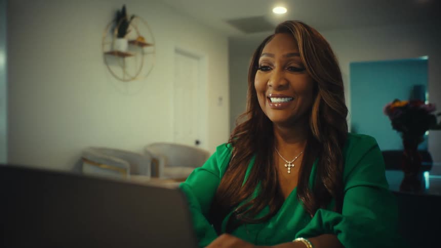 A cinematic slow-motion reveal shot shows a happy businesswoman in her home office celebrating good news on her laptop