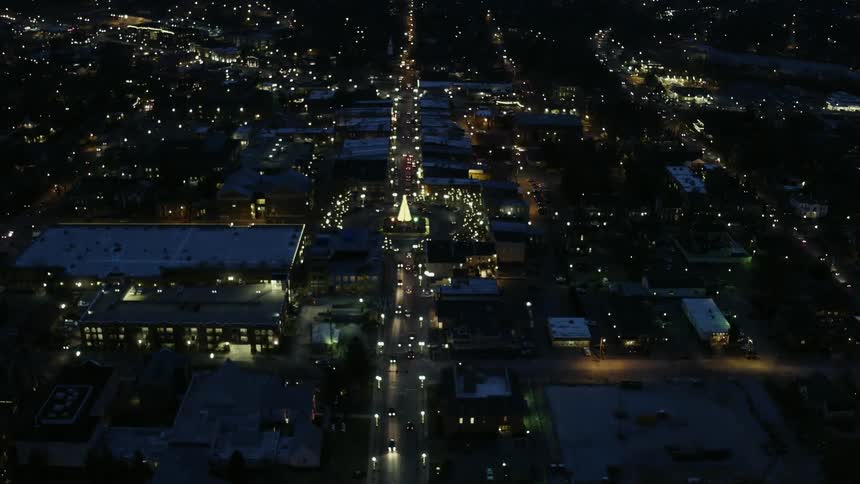 Vehicles travel down a parkway toward a lighted tree in a roundabout at night