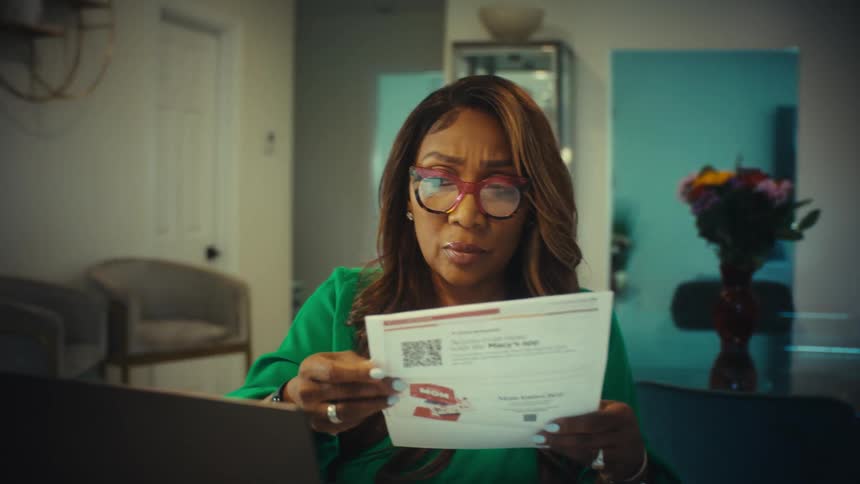 A concerned woman puts on her glasses while looking over her bills and financial data on a laptop at home
