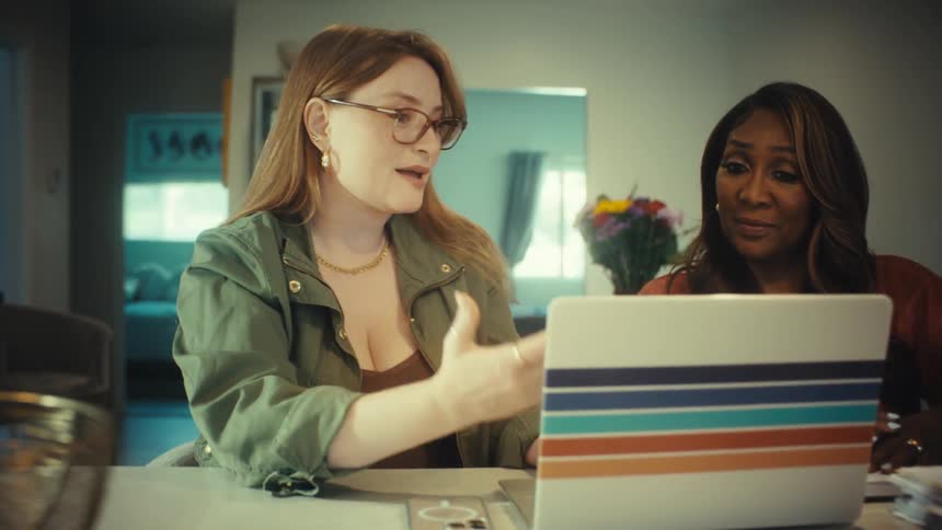 Two diverse female colleagues collaborate on a project, pointing at a laptop screen while working from a modern home