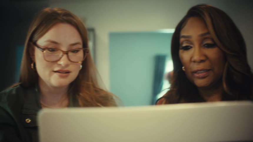 Close up dolly shot of two diverse professional women collaborating over a laptop in their office
