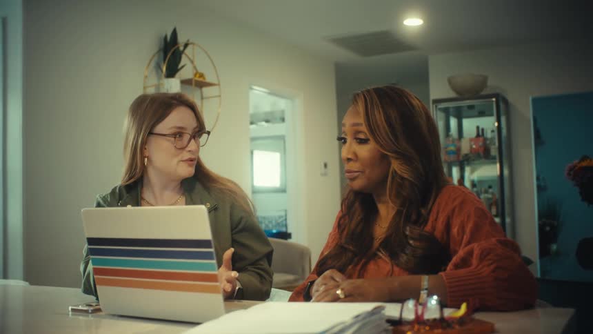 Two professional women have an exciting discussion while reviewing information on a laptop in a modern home