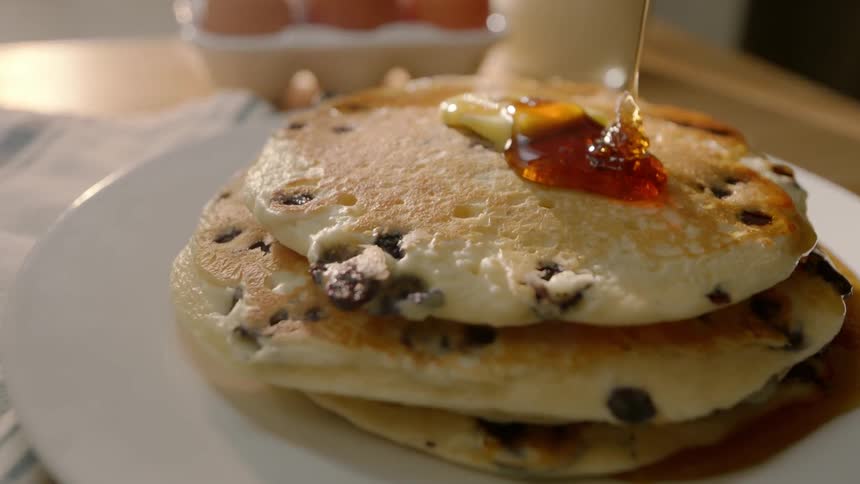 Syrup is poured onto a stack of pancakes