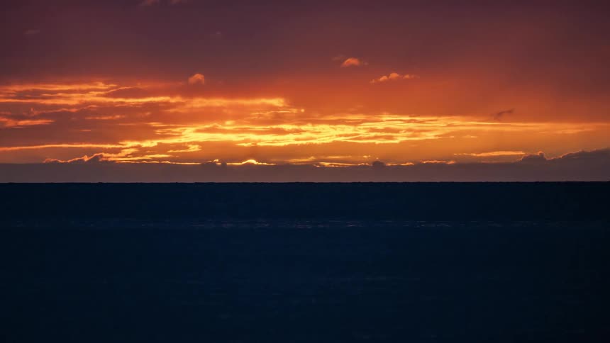 A timelapse of a brilliant orange sun dipping below the horizon as it sets over the vast, dark ocean