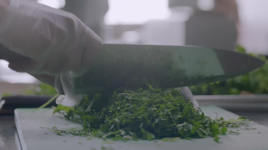 A restaurant worker dices green herbs on a cutting board