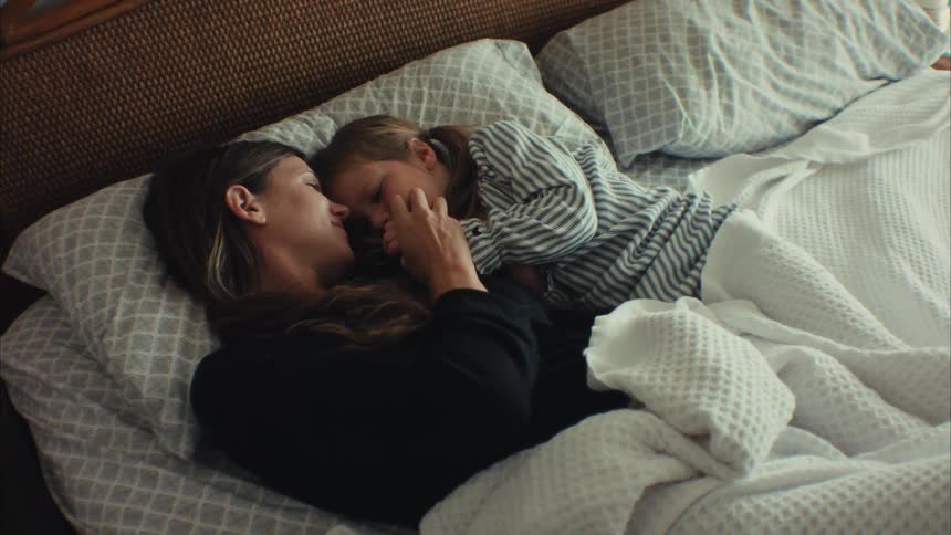 A mother and her young daughter share a peaceful and loving moment while cuddling in bed together