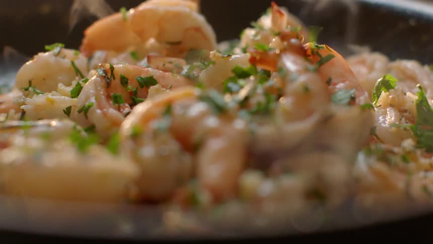Parsley is poured on cooking shrimp in a pan