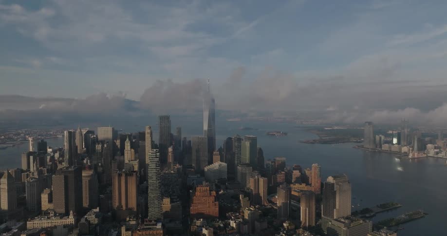 Static aerial view of the Lower Manhattan skyline with One World Trade Center emerging through the morning clouds