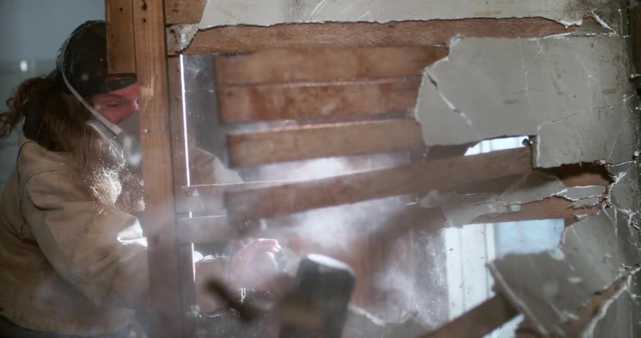 A construction worker smashes a plaster wall with a sledgehammer in extreme slow motion