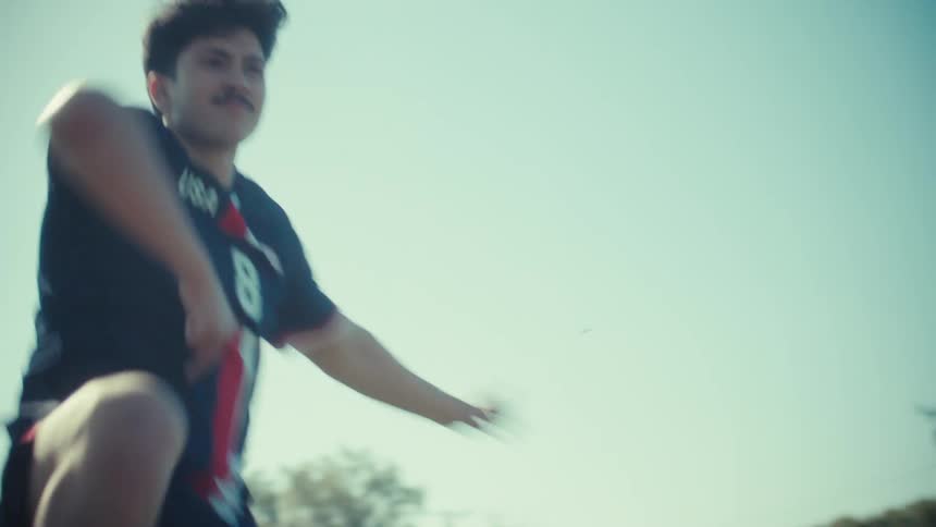 A smiling soccer player in a USA jersey celebrates as he runs in slow motion across a sunny field
