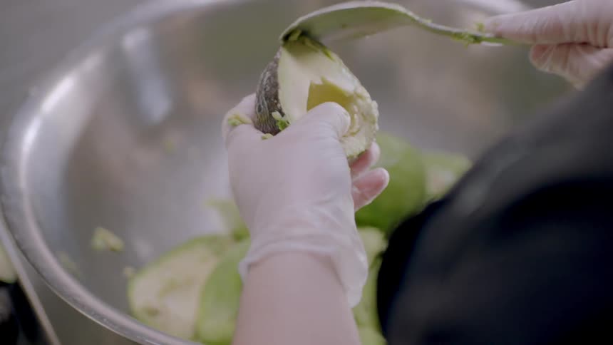 A person is scooping out avocados into a bowl