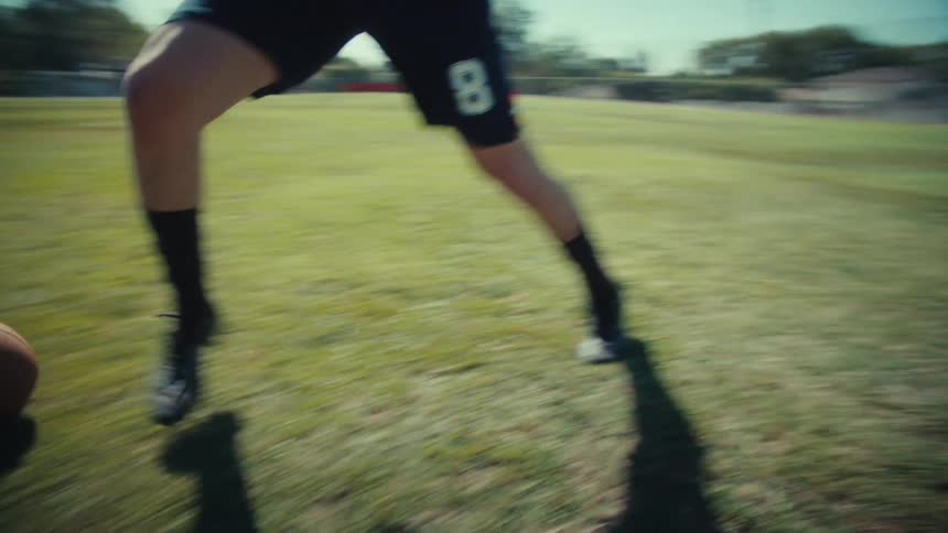 Slow-motion shot of a young male athlete skillfully dribbling a classic soccer ball on a sunny day