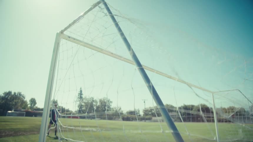 Slow motion shot of a soccer ball hitting the back of the net after a powerful kick on a sunny field