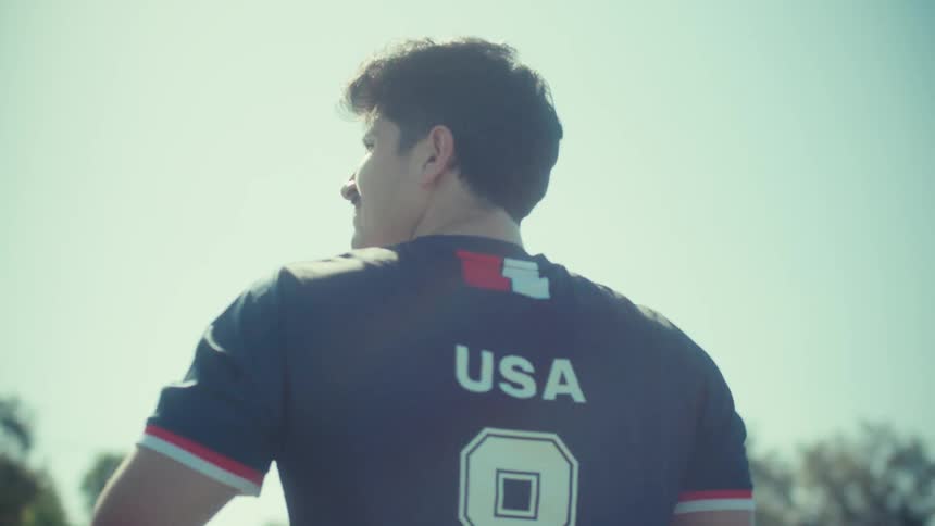 An epic slow-motion shot from behind a USA soccer player as he walks with a ball into the bright, flaring sunlight