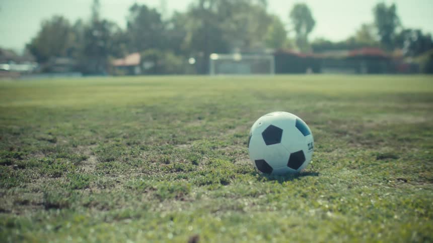 A slow push in on a lone soccer ball resting in the middle of a grassy field on a sunny day
