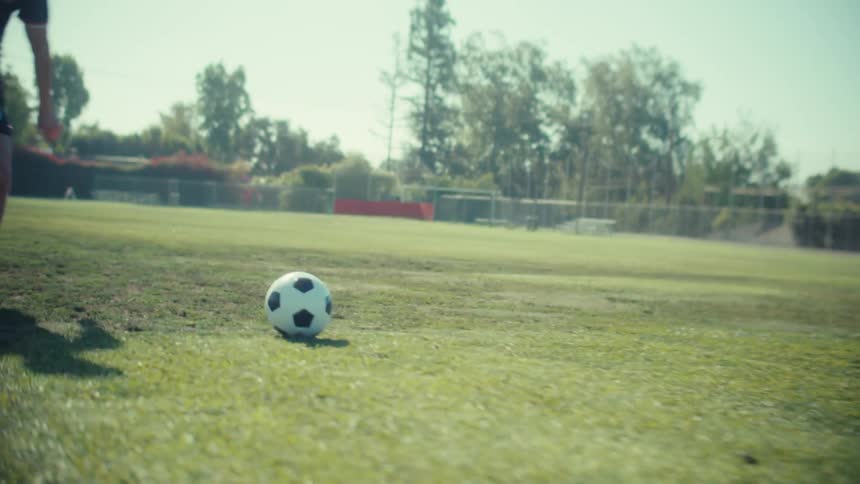 Slow motion close-up of a soccer player's powerful kick on a sunny practice field