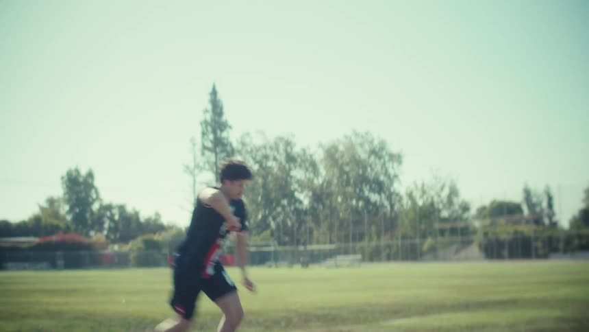 A male soccer player in a USA jersey kicks a ball on a green field in slow motion on a sunny day