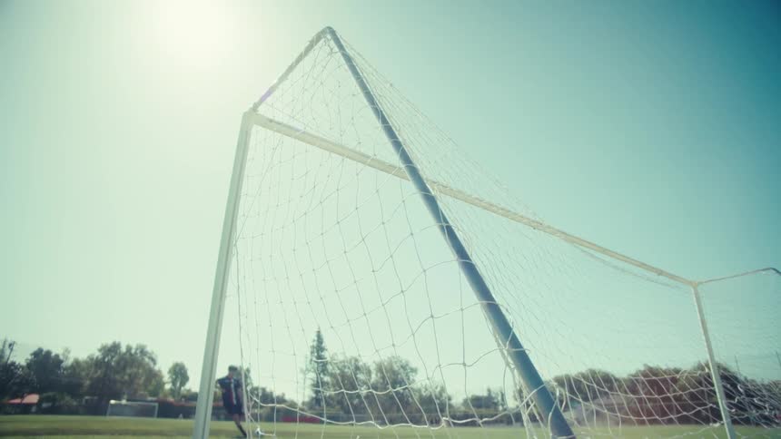 Slow-motion close-up of a soccer ball flying into the goal net on a sunny day
