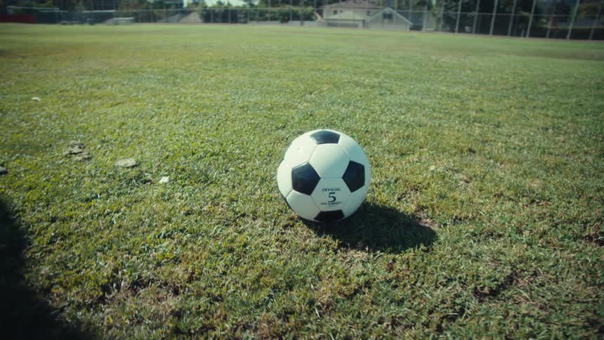 Cinematic slow motion of a soccer player setting up the ball on a sunny field before running up and kicking it with power