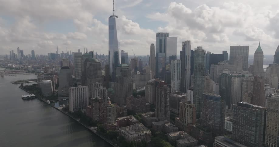 An epic aerial push-in shot showcases the downtown Manhattan skyline and One World Trade Center from across the Hudson River on a partly cloudy day